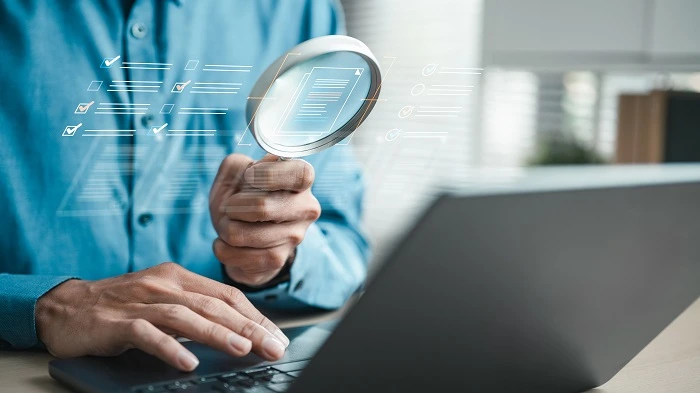 Hombre revisando documentos en una computadora portátil con una lupa